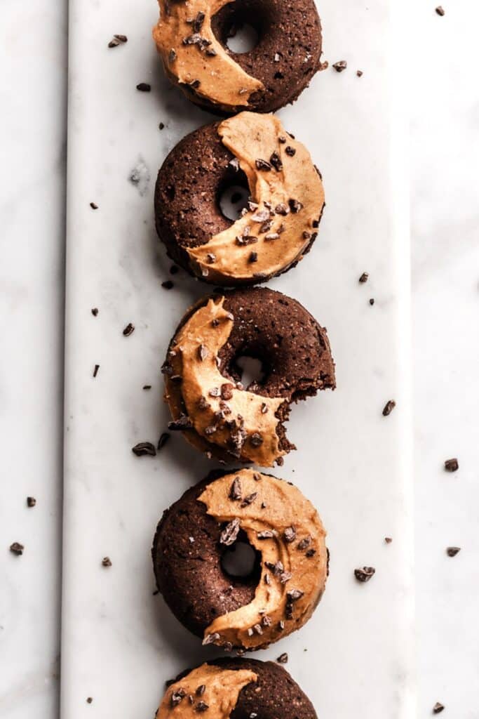 Chocolate baked donuts on a marble board in a straight line with pumpkin frosting on half of them. 