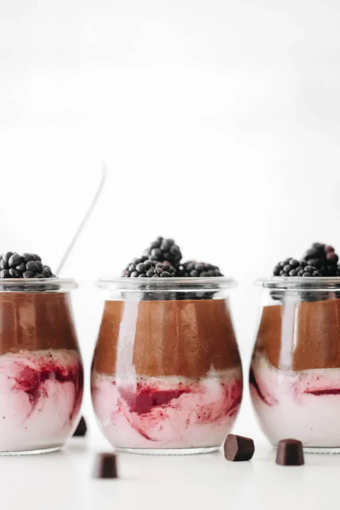 Clear glass jars with blackberry cream on the bottom and chocolate mousse on top with fresh berries.