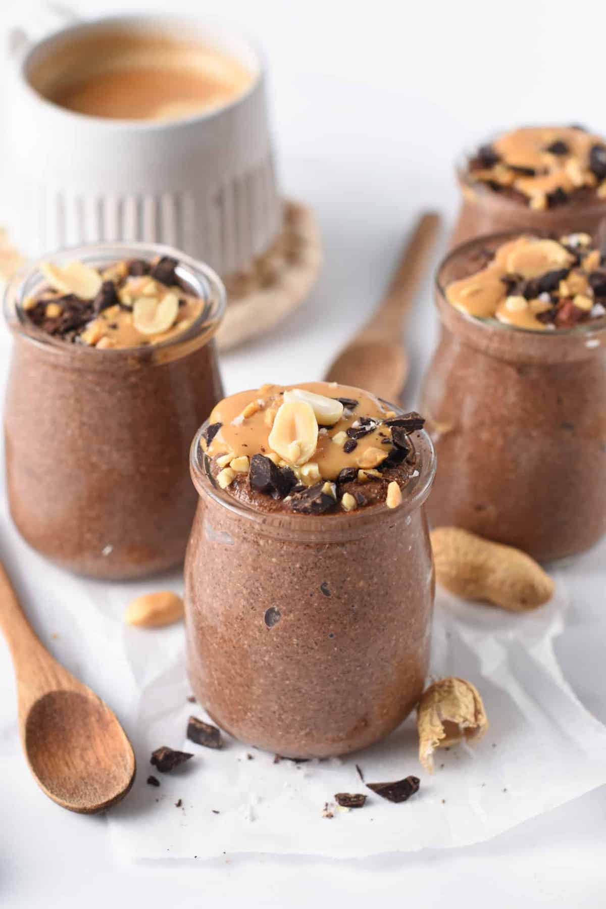 Several glass jars filled with chia pudding topped with chocolate chunks, peanuts, and pb drizzle.