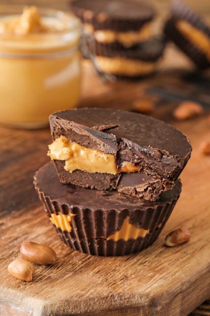 Chocolate peanut butter cups stacked two tall with the top one broken in half showing the inside. 