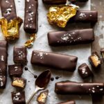 Several homemade twix bars laid out on parchment paper with finishing salt sprinkled on top.