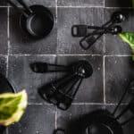 Black measuring spoons and measuring cups on black tile with silver grout.