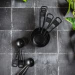 Black measuring cups and spoons on black tile.
