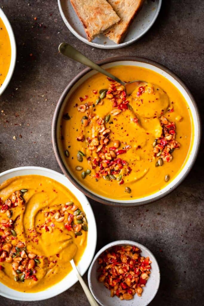 Two large bowls of pumpkin soup with pumpkin seeds and pomegranate arils on top.