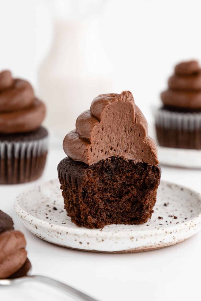 Chocolate cupcakes topped with chocolate frosting on a white speckled plate.