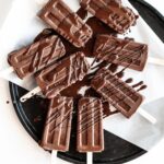 Eight vegan fudge pops on a black plate drizzled in chocolate.
