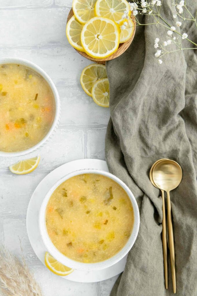 Two bowls of vibrant yellow lemon soup with a gold spoon and linen napkin.