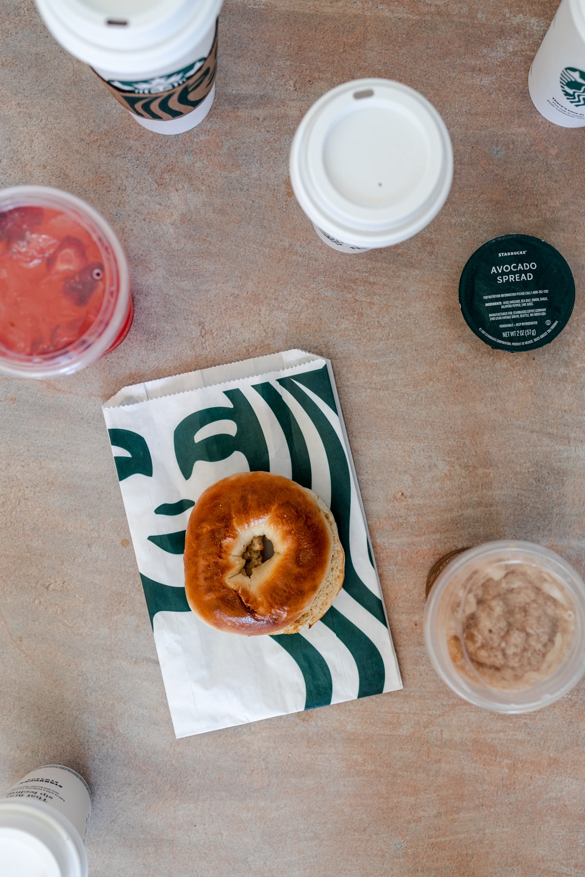 Plain bagel on a starbucks paper bag with cups around.