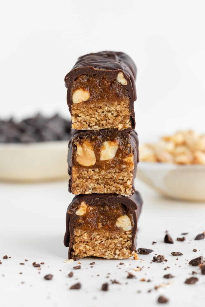 Three vegan snickers stacked on top of each other with the end cut off so you can see the layers inside. 