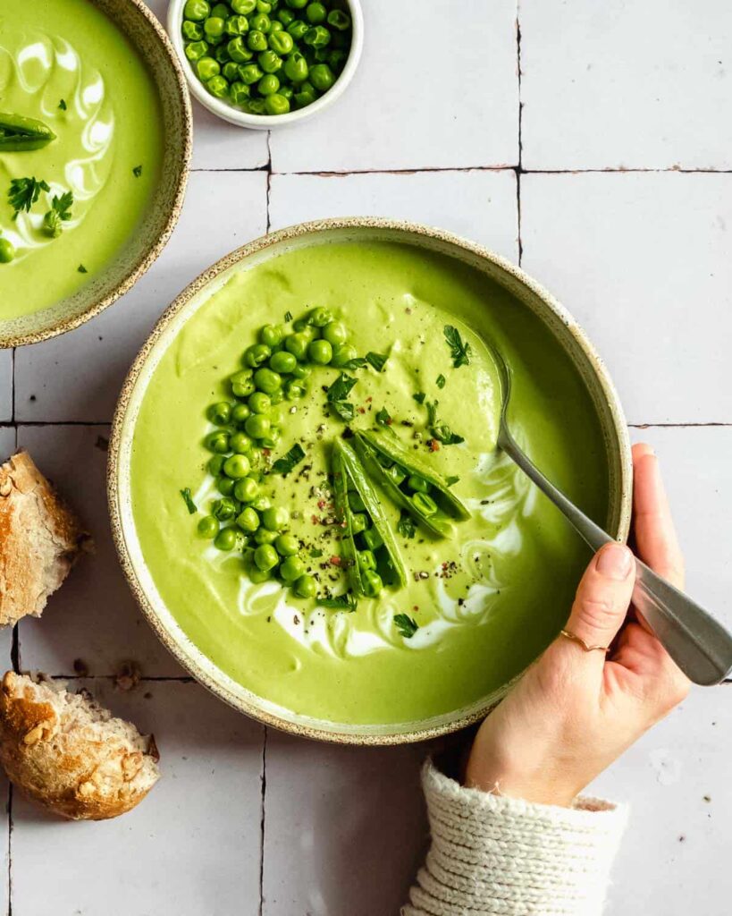 Large bowl of green colored soup with a spoon in it held by a woman.