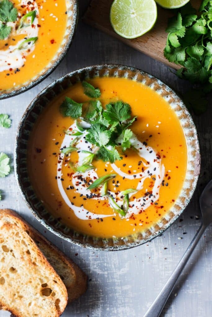 Striped bowl of pumpkin soup with coconut cream swirl and leafy greens on top.