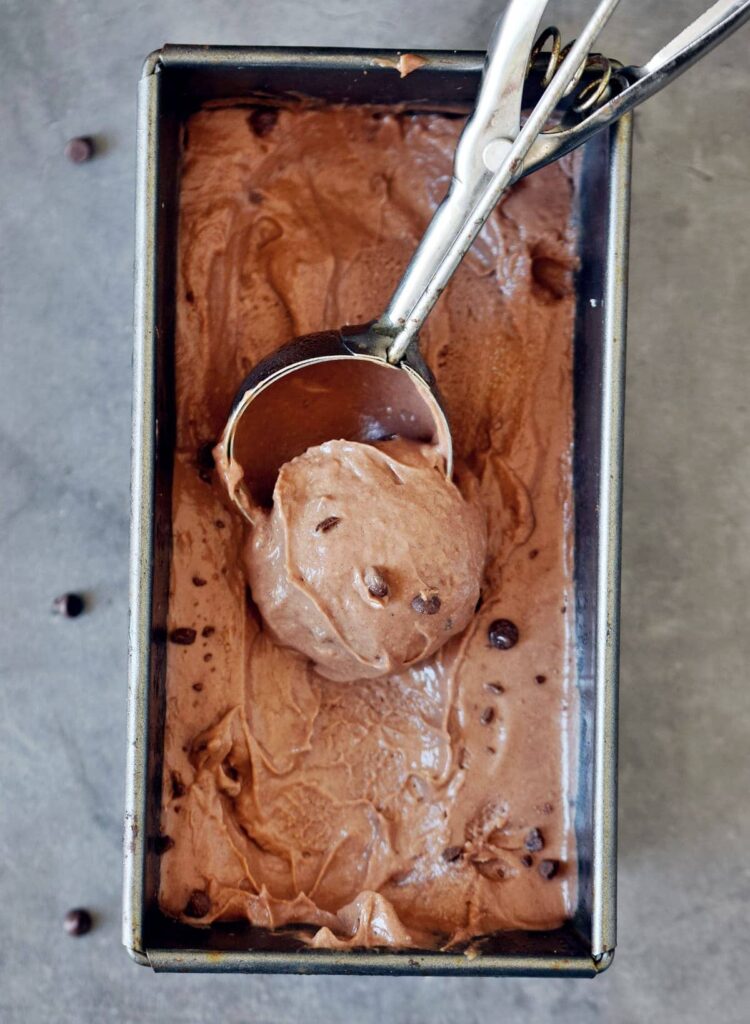 Metal loaf pan filled with vegan chocolate ice cream and an ice cream scoop scooping some out. 