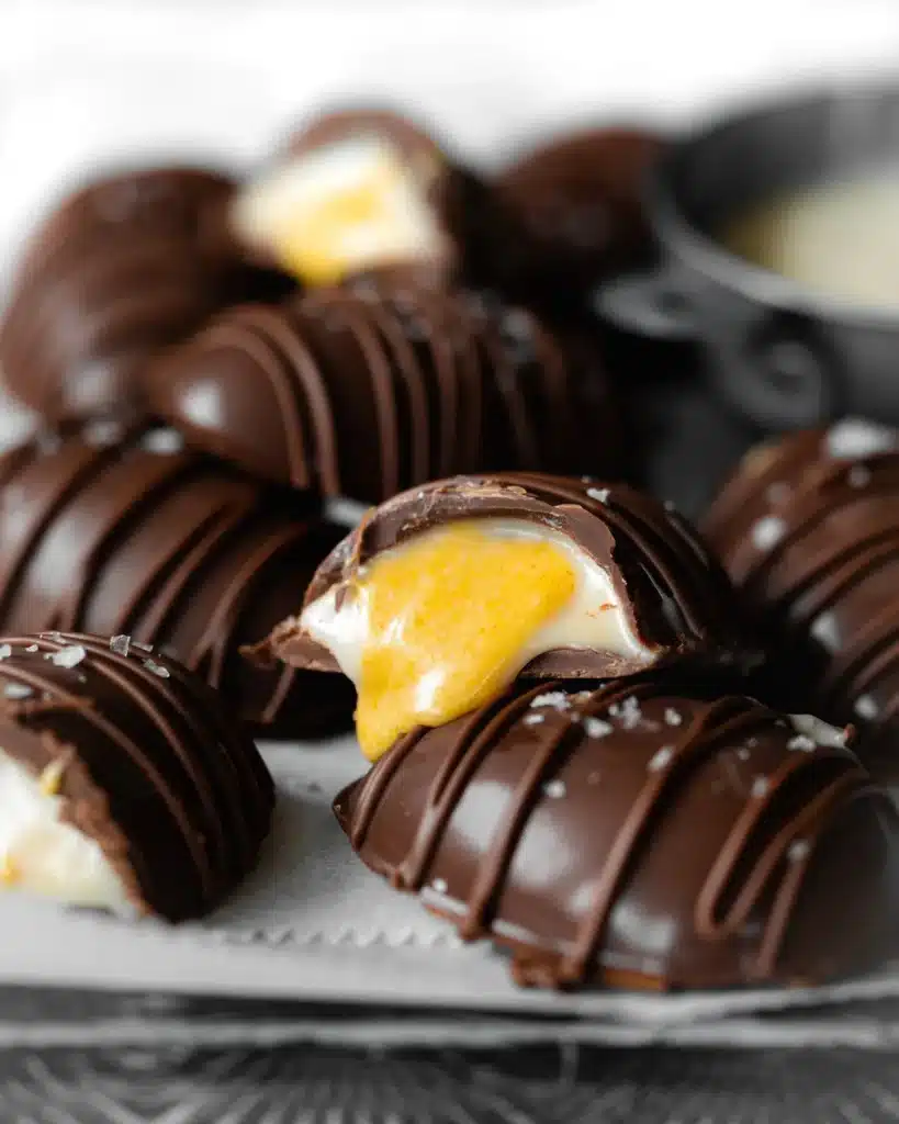 Several chocolate creme eggs with a couple cut in half showing the creamy center.