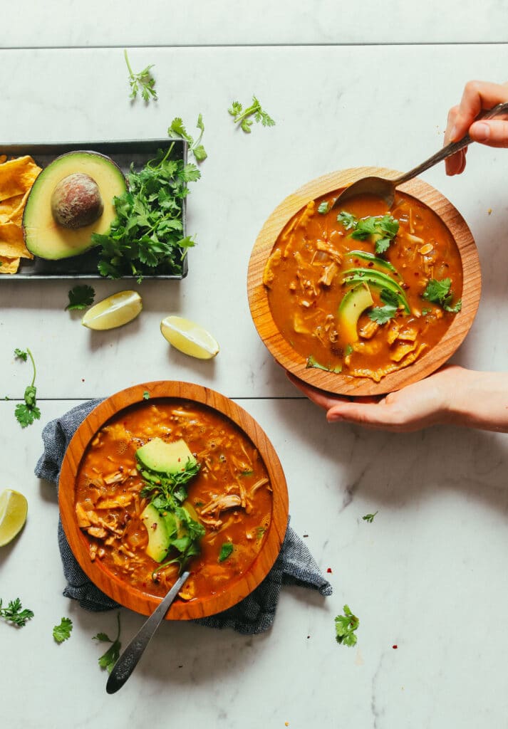 Two wooden bowls filled with tortilla soup topped with tortilla chips, avocado, and cilantro.