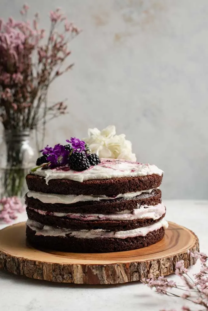 Four layered chocolate cake with fresh flowers and blackberries on top. 