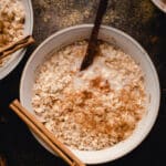 White ceramic bowl filled with cinnamon brown sugar oats with a cinnamon stick resting on the rim.