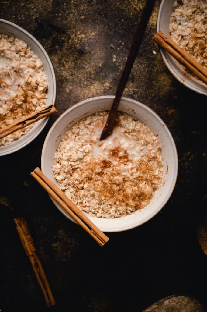 One bowl of cinnamon oatmeal with two other bowls on the edges.