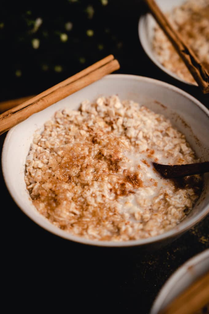 Close up angle of cinnamon oats in a white bowl with a wooden spoon.