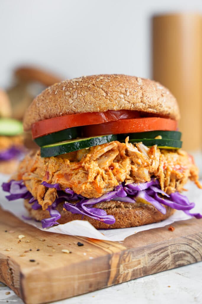 Buffalo pulled jackfruit with fresh red cabbage, cucumber and tomato sliced on a bun.