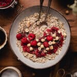 Top down photo of chia oats with fresh raspberries hazel nuts on top surrounded by ingredients.