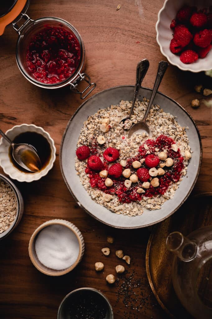 Ceramic bowl filled with oatmeal surrounded by its ingredients and toppings.