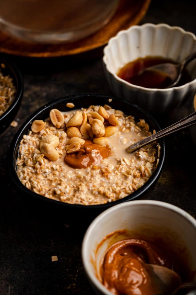 Peanut butter oatmeal in a black ceramic bowl with peanuts and peanut butter on top.