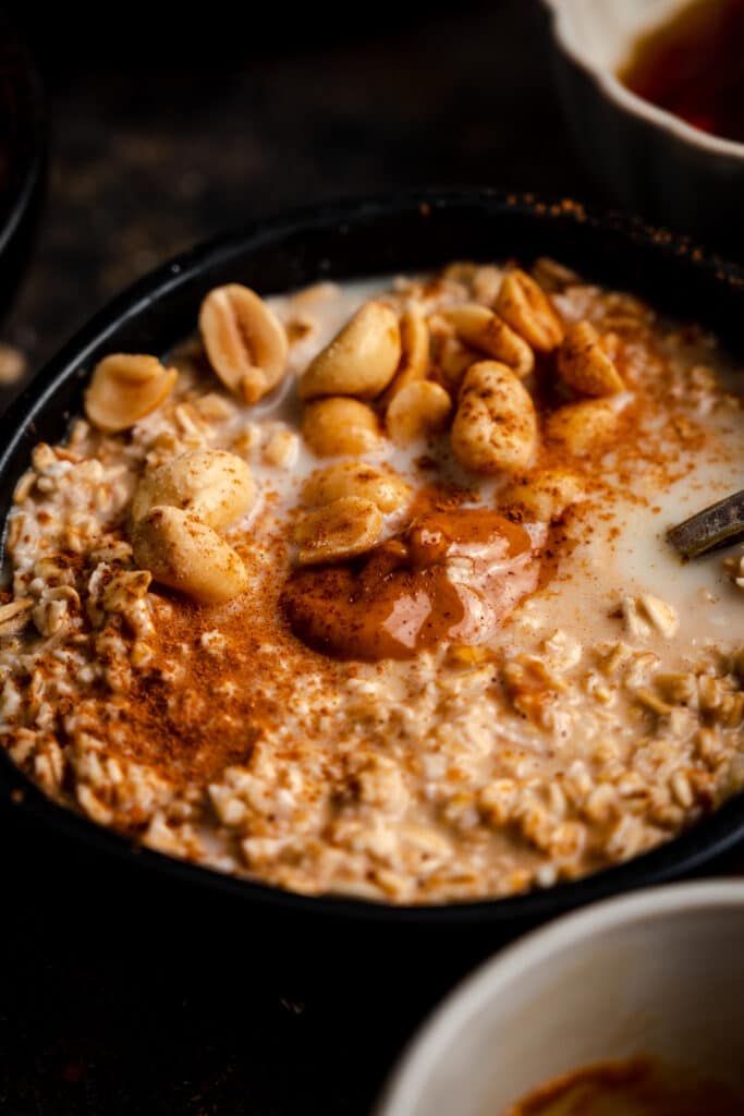 Close up of oatmeal in a black bowl with peanut butter and peanuts on top.