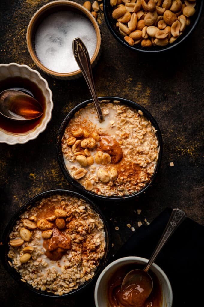 Flatlay of two bowls of peanut butter oatmeal with bowls of its ingredients surrounding it.