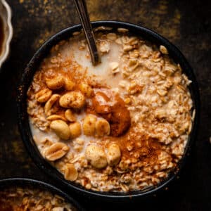 Close up of peanut butter old-fashioned oatmeal in a black bowl with a spoon sticking out of it.