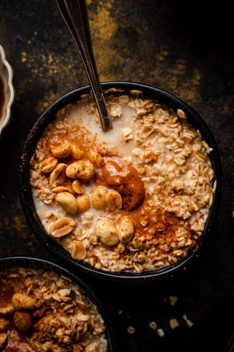 Close up of peanut butter old-fashioned oatmeal in a black bowl with a spoon sticking out of it.