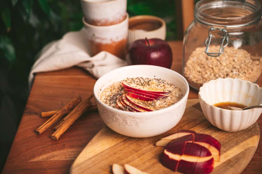 Wooden table with ingredients for gluten-free oatmeal and a big bowl of apple cinnamon oats.