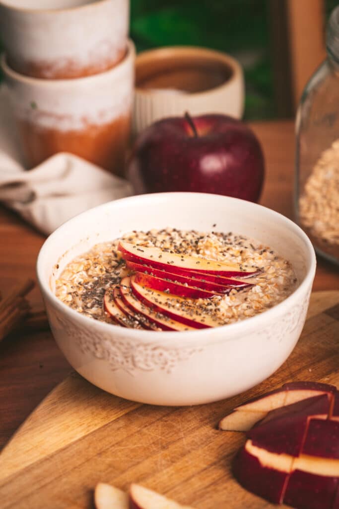 Apple cinnamon oats in a white bowl with sliced apples next to it.