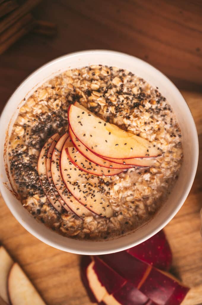 Close up of apple cinnamon oats in a bowl with chia seeds, apples slices, and maple syrup.