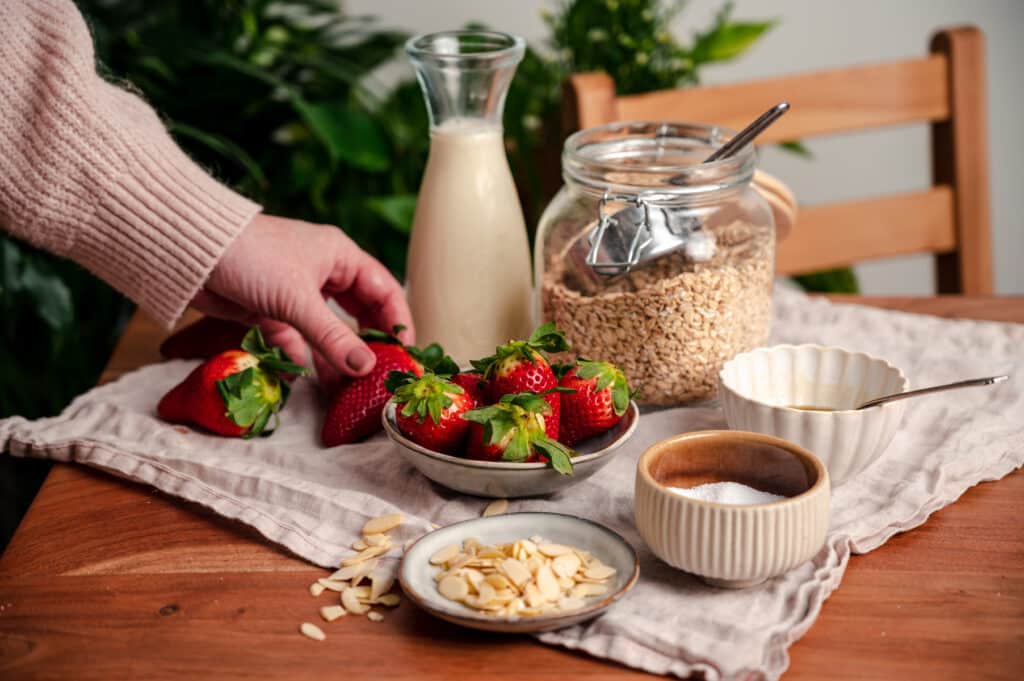 Ingredients for strawberry oats with a woman placing strawberries on the table.