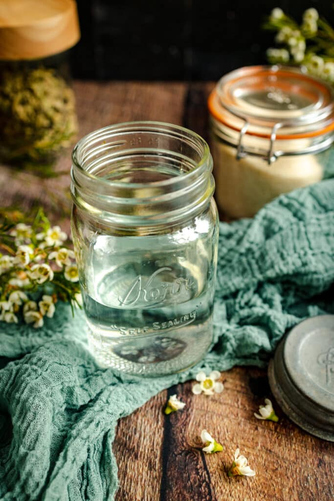 Angle view of half filled glass pint jar on a teal cloth with flowers around it.