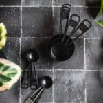 Black tiles with silver grout with a stack of black measuring cups and spoons.