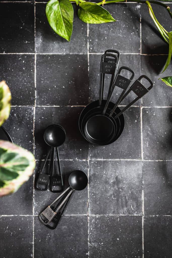Black tiles with silver grout with a stack of black measuring cups and spoons.