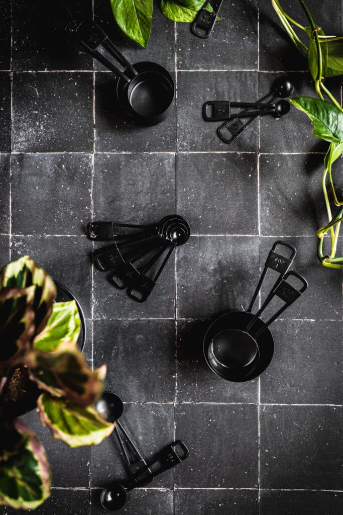 Black tile surface with black measuring cups and measuring spoons.
