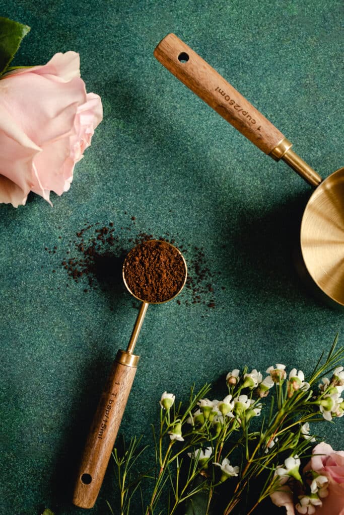 Wood and gold tablespoon with ground coffee overflowing onto the green surface.