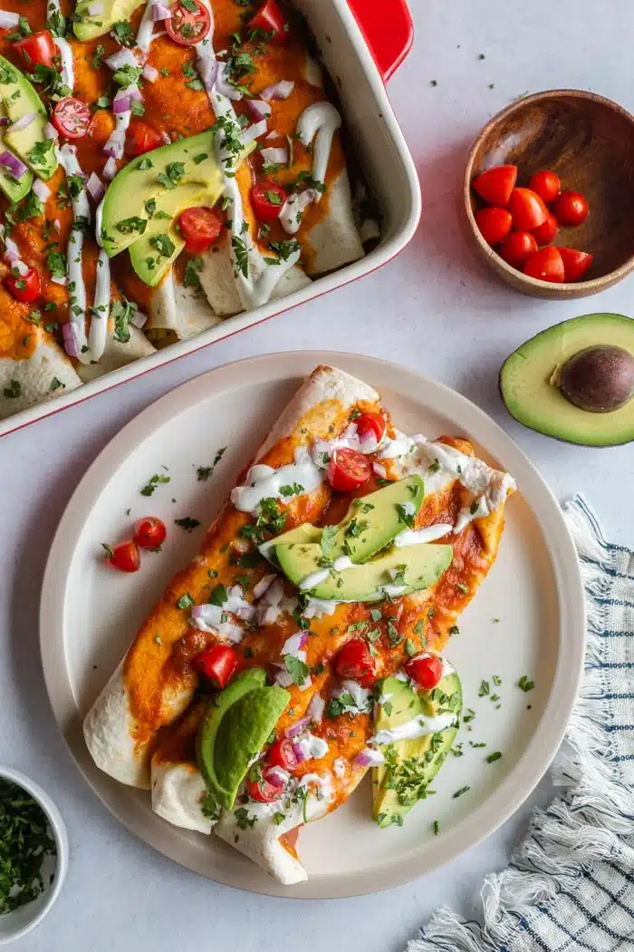 Plate with two enchiladas on it with sliced avocado on top.