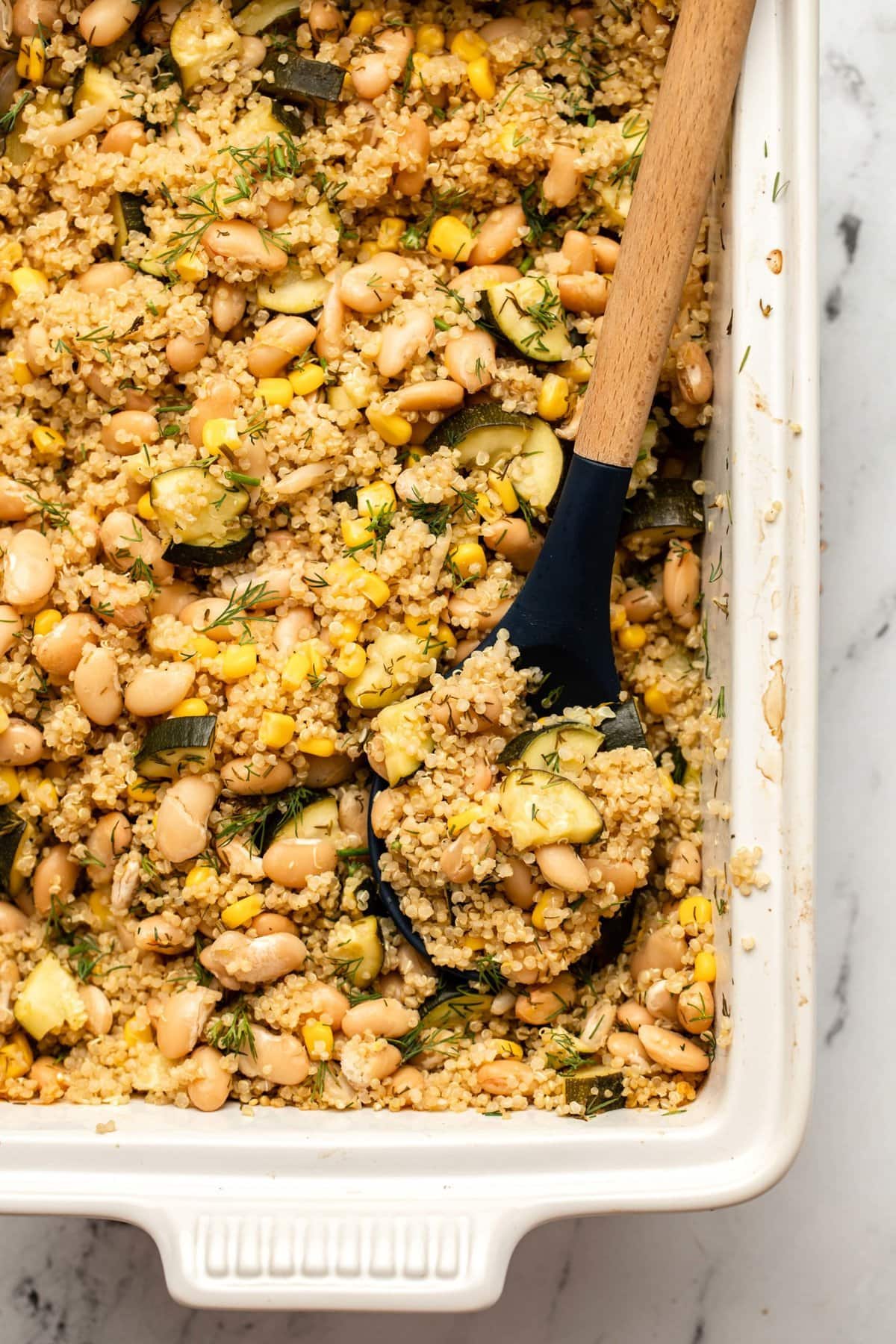 A white baking dish filled with 60 vegan casserole recipes featuring quinoa, zucchini, and corn.