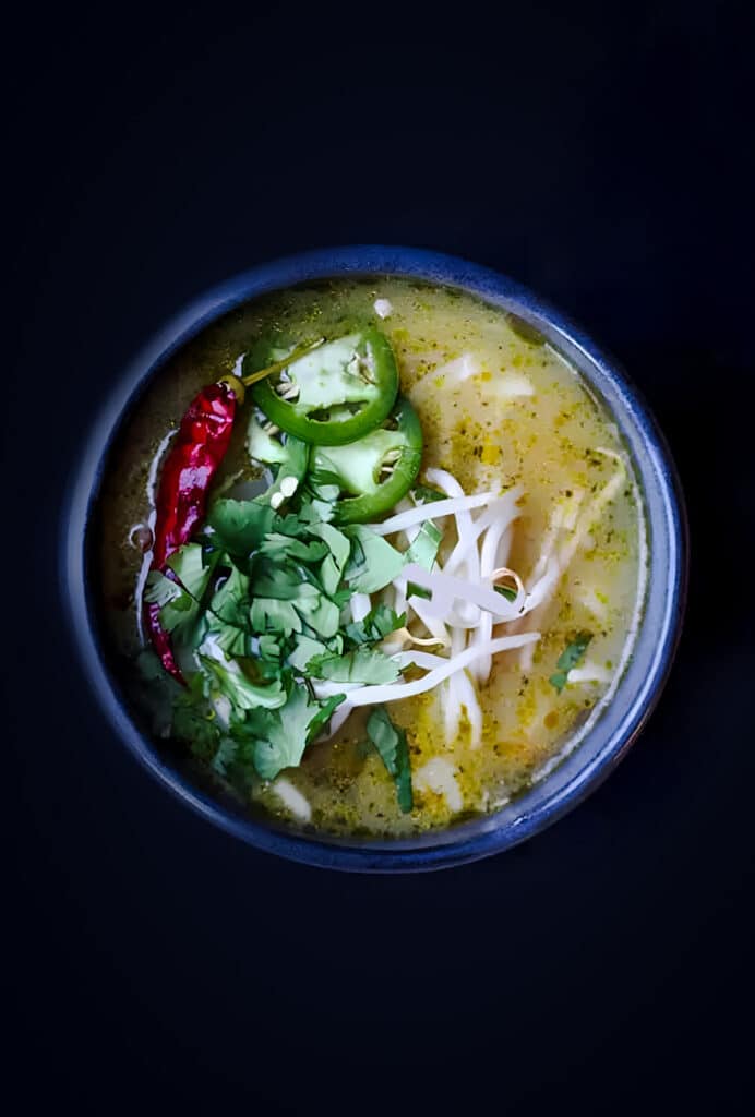 Black bowl of broth rice noodle soup topped with bean sprouts, sliced jalapeño, and cilantro.