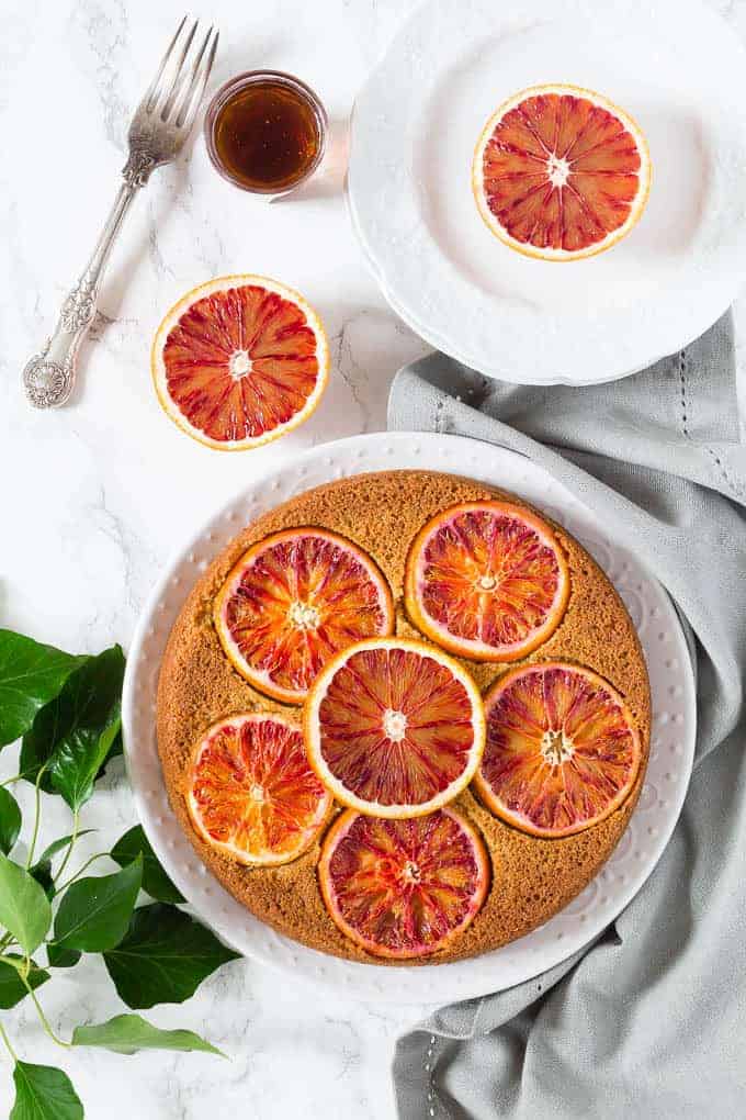 Olive oil cardamom and blood orange polenta cake on a decorative white serving plate.