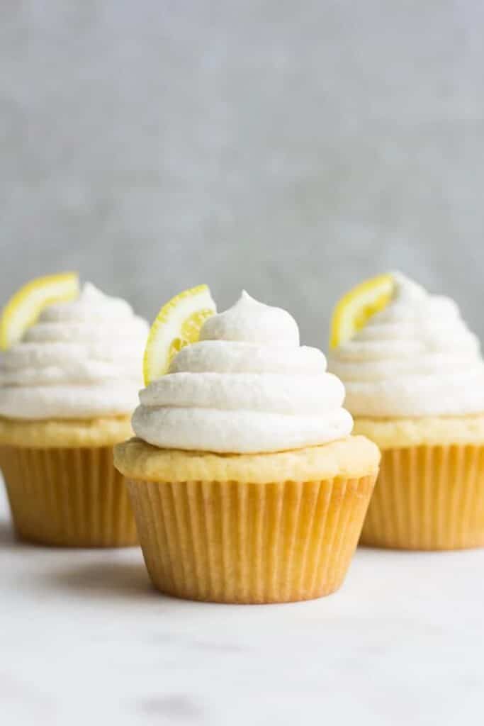 Three lemon cupcakes topped with lemon buttercream frosting and a slice of lemon.