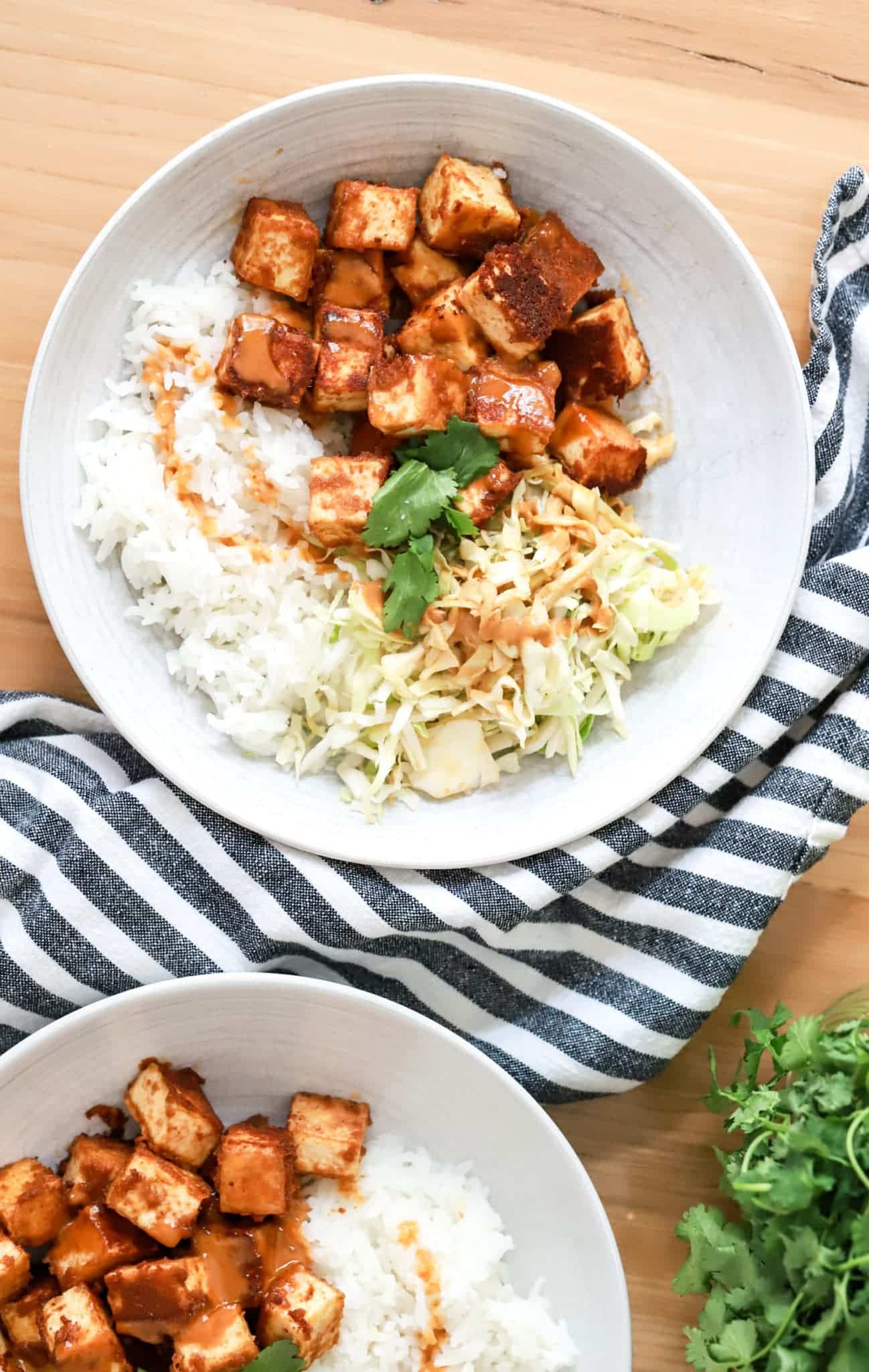 Two vegan bowls of tofu and rice on a wooden table.