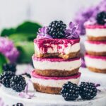 Brown, white, and pink, mini blackberry cheesecakes stacked on top of each other.