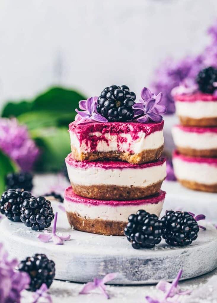 Brown, white, and pink, mini blackberry cheesecakes stacked on top of each other.