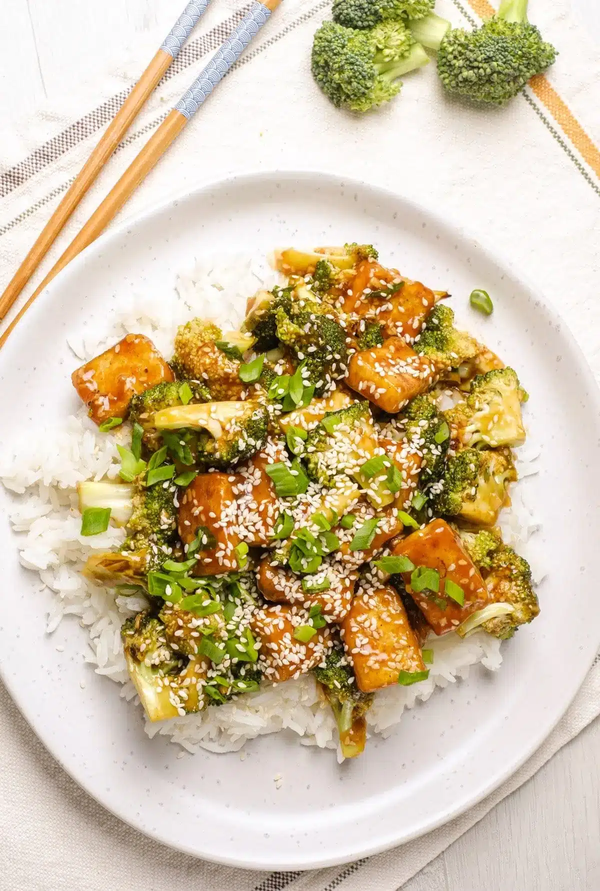 A vegan white plate with tofu, broccoli, rice and chopsticks.
