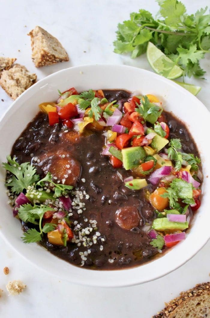 A vegan black bean soup cooked in a crockpot and served with vegetables and bread.