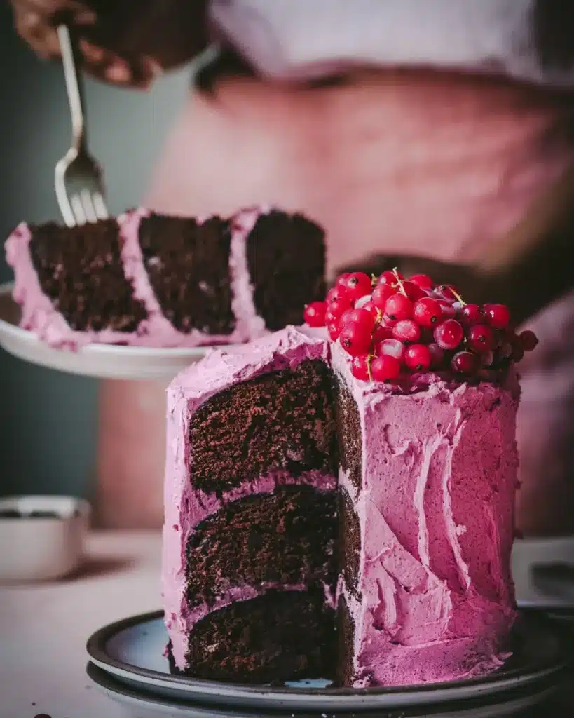 Chocolate cake with pink frosting and a slice cut out. 